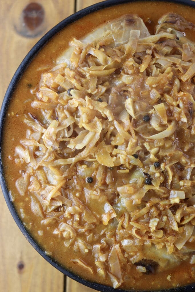 Half baked stuffed cabbage rolls covered with sauce in a baking pan.